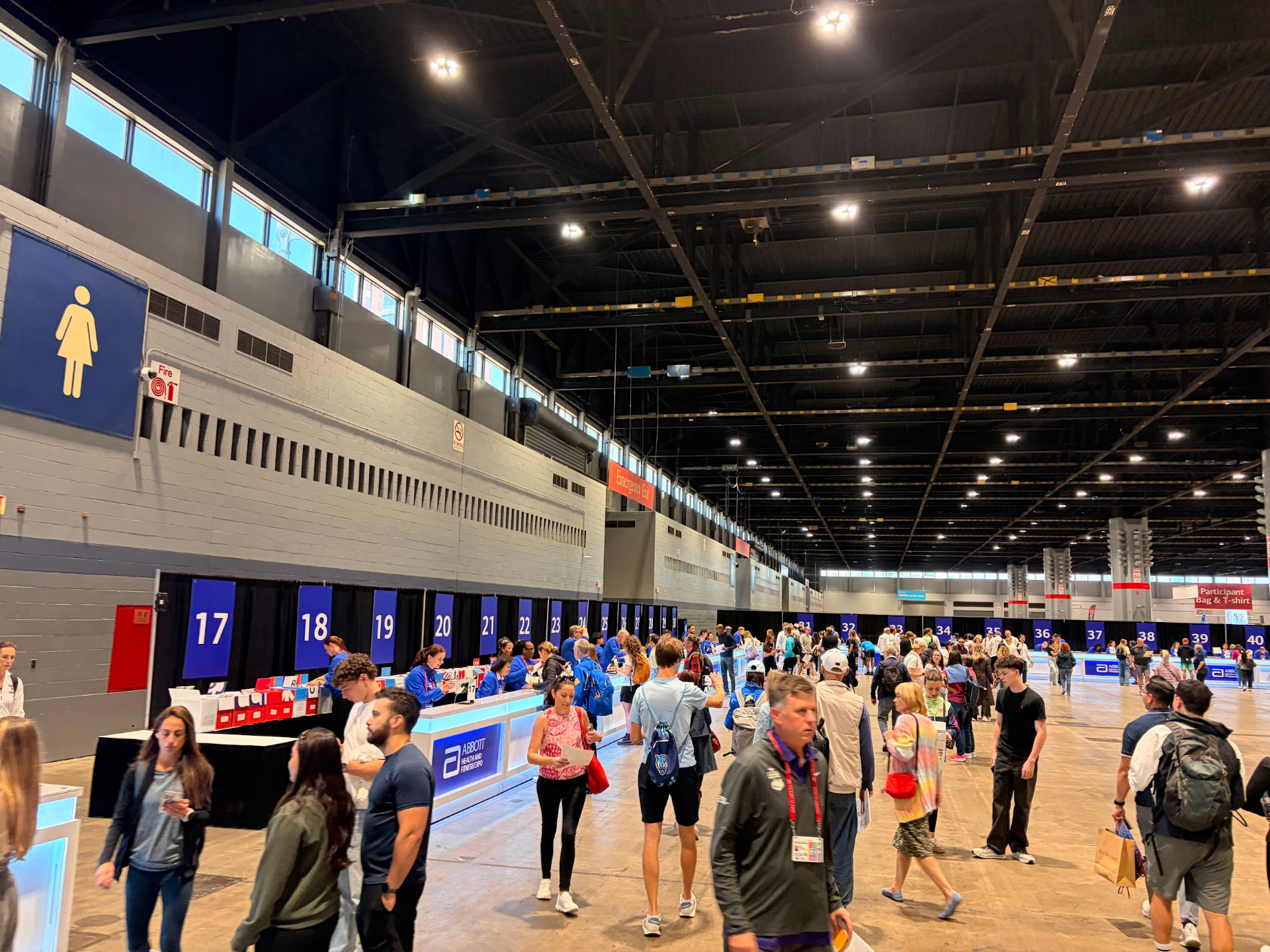 Numbered packet distribution desks running along the wall at the 2026 Abbott Health and Fitness Expo, with a Participant Bag and T-shirt sign at the far end