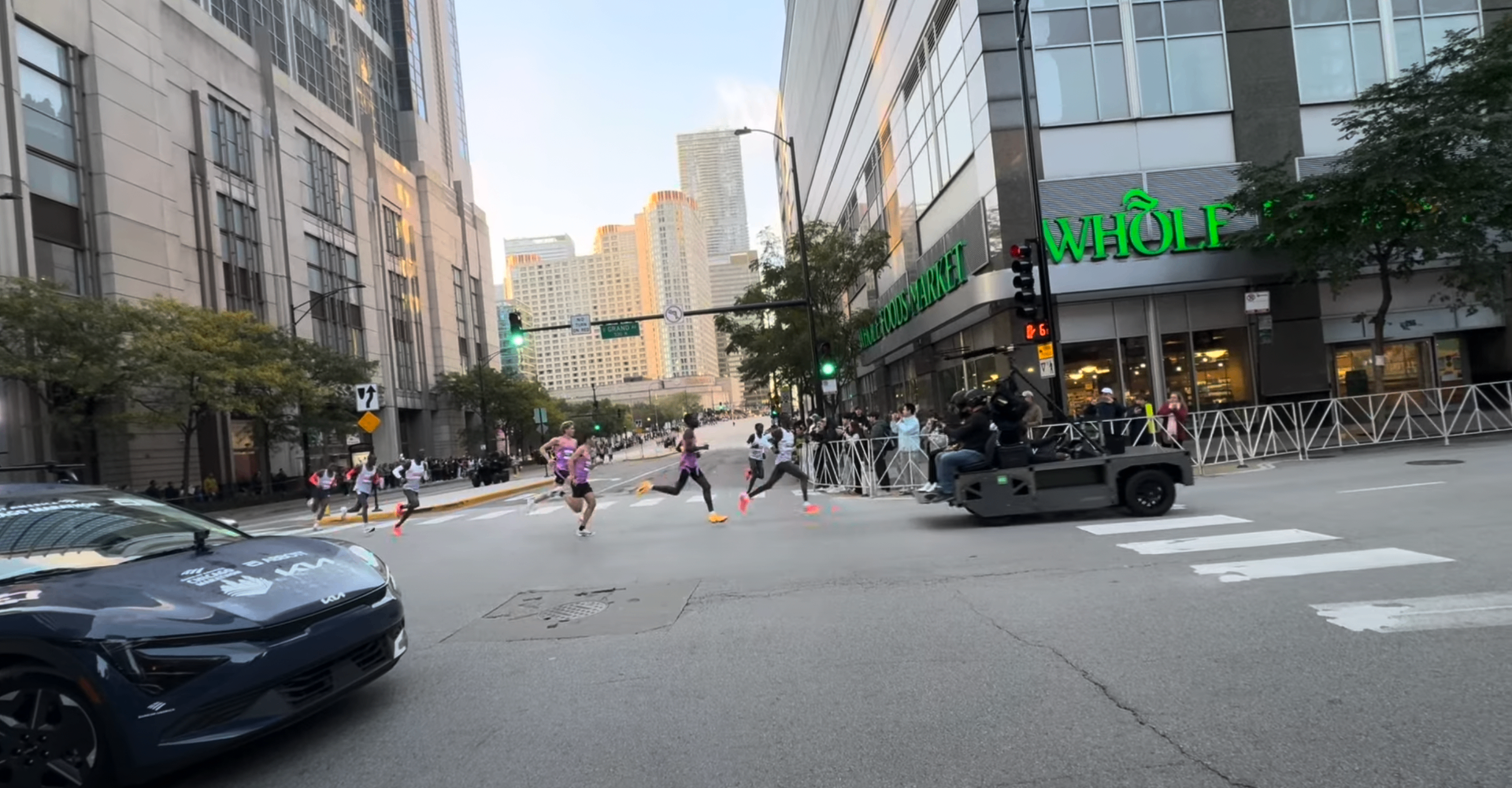 Elite runners making the turn onto Grand Avenue past Whole Foods with the downtown Chicago skyline in the background and a camera truck following